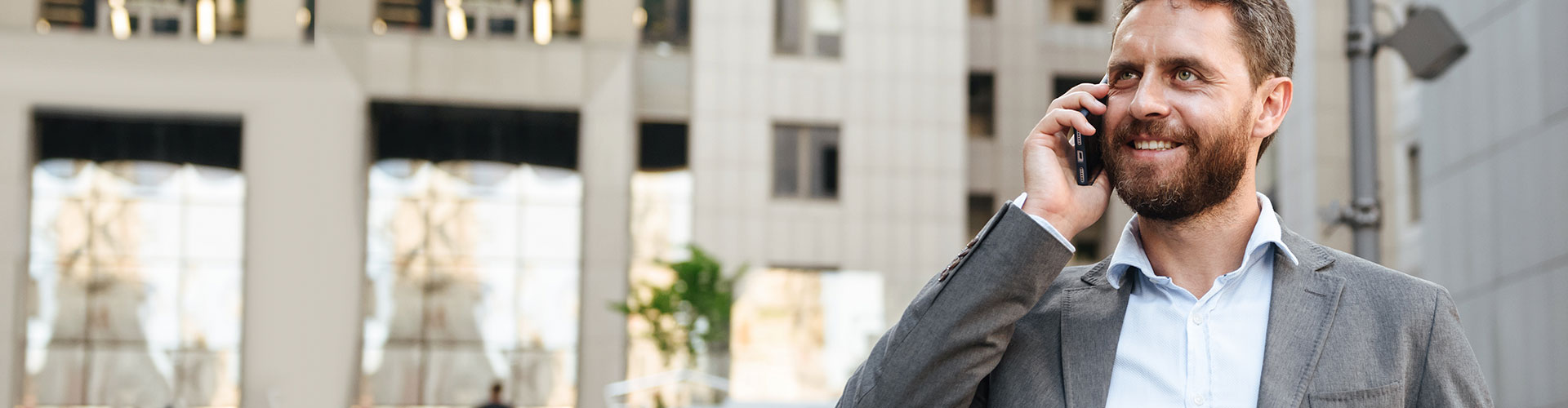 Seguros Banca Privada - Hombre de negocios con un traje gris y camisa blanca hablando por el móvil junto a un edificio en una ciudad Seguros Banca Privada - Hombre de negocios con un traje gris y camisa blanca hablando por el móvil junto a un edificio en una ciudad