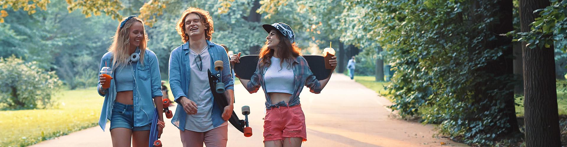 Cuenta Joven Up - Grupo de jovenes vestidos con ropa moderna con patinetes, sonriendo junto a un parque rodeado de arboles