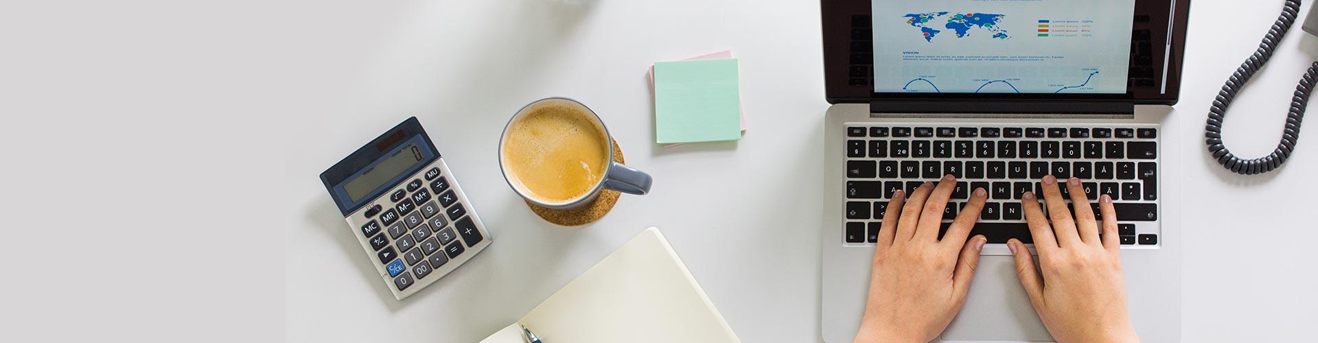 Operaciones en divisas - Mesa de despacho con una calculadora, una taza de café, un bloc de notas, un teléfono y un portátil