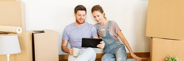 Hipoteca Vivienda - Una pareja sentada en el suelo entre cajas de mudanza con una tableta digital Hipoteca Vivienda - Una pareja sentada en el suelo entre cajas de mudanza con una tableta digital